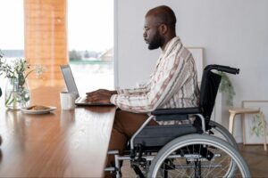 Man using laptop while sitting in wheelchair at home office, representing long-term disability and divorce financial planning